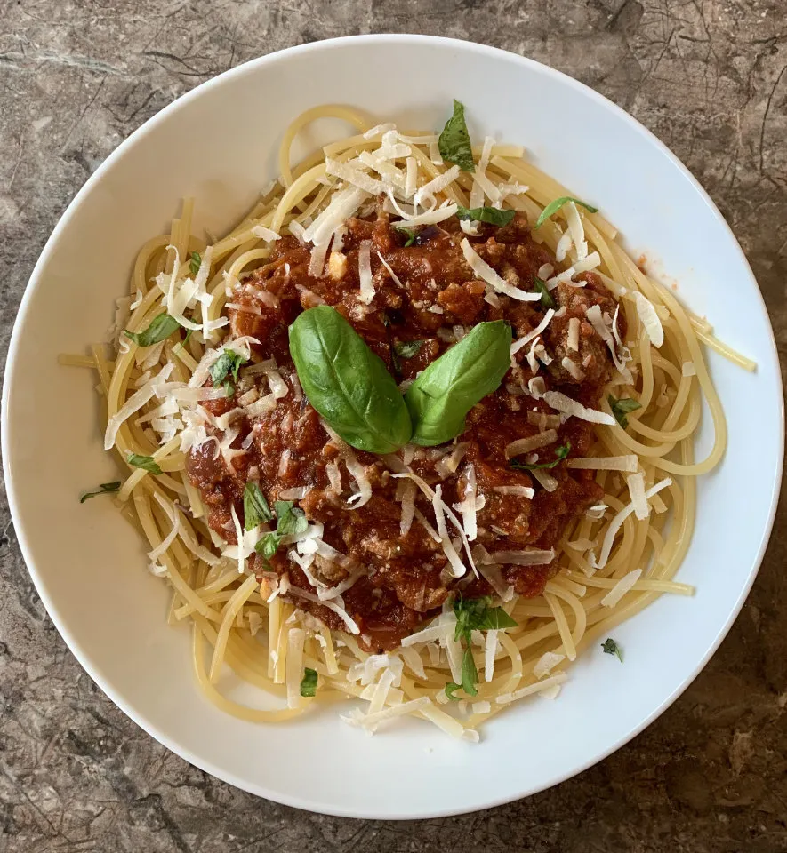A bowl of spaghetti with meat sauce and basil.